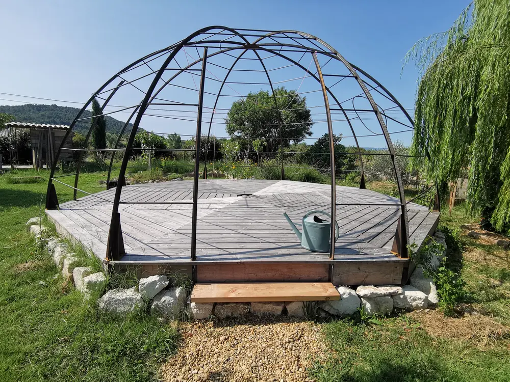 Structure métallique arrondie de l’Igloo Végétal au-dessus d’une terrasse en bois