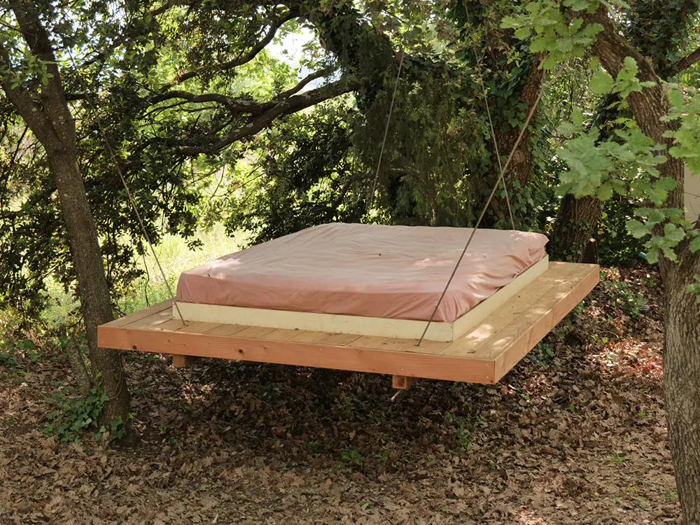 Lit suspendu en bois avec matelas, accroché aux branches dans une clairière