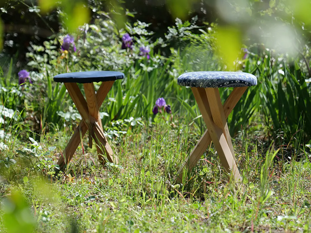 Tabourets en bois à pieds croisés avec assise en tissu, posés dans un jardin